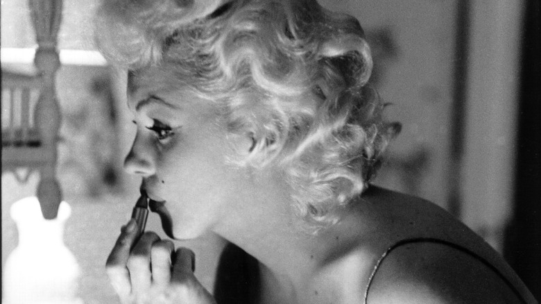 Marilyn Monroe applying her lipstick while looking in a mirror