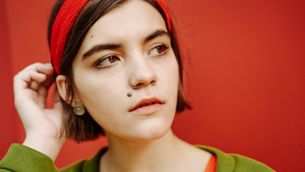 A woman with a mole on her face touched her hair while looking sideways.