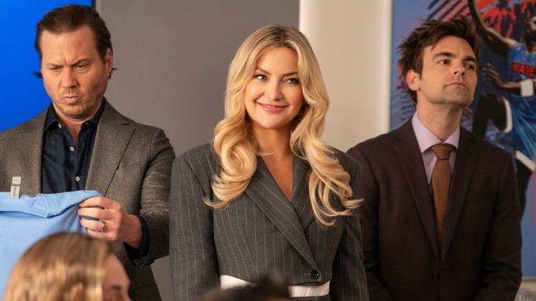 Scott MacArthur, Kate Hudson, and Drew Tarver standing at a table of executives in Running Point