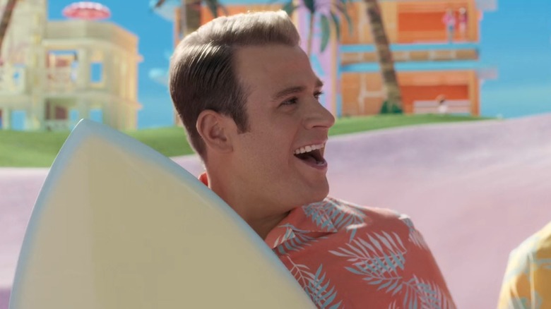 Scott Evans holding a surfboard on the beach in Barbie