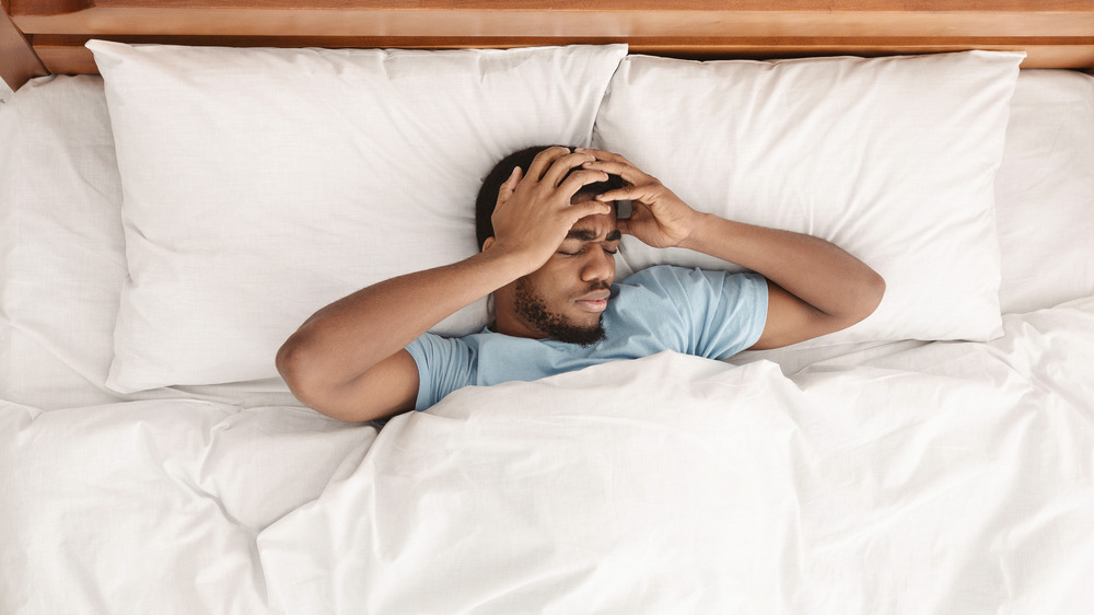 Man in bed clutching his head