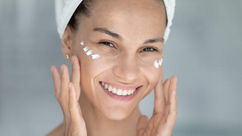 A smiling woman applying moisturizer under her eyes