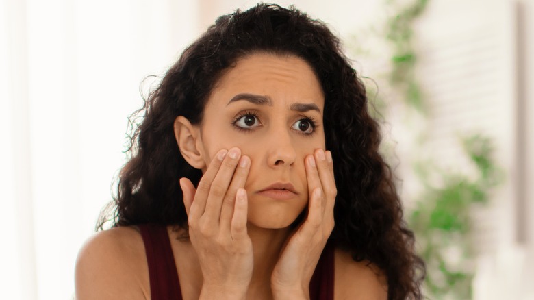 A woman looks in the mirror while touching her face