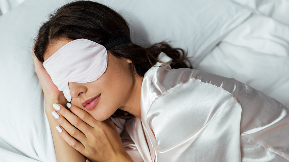 Dark haired woman sleeping on a white pillow with a sleep mask. 