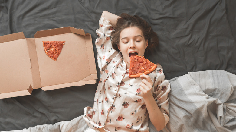 A woman eating pizza in bed