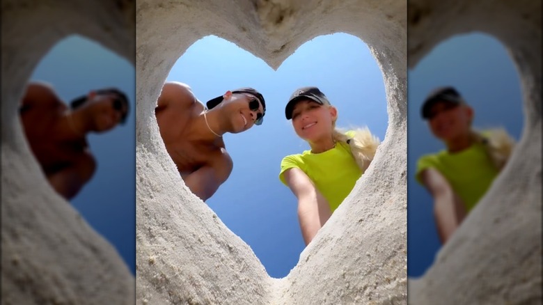 Dale Moss smiling at Galey Alix (photo taken through heart-shaped hole in the sand)