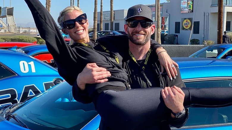 Tarek El Moussa and Heather Rae Young smiling in front of race cars