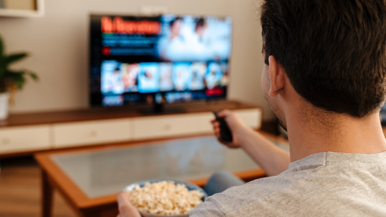 Man pointing at a TV with a remote control holding a bowl with popcorn