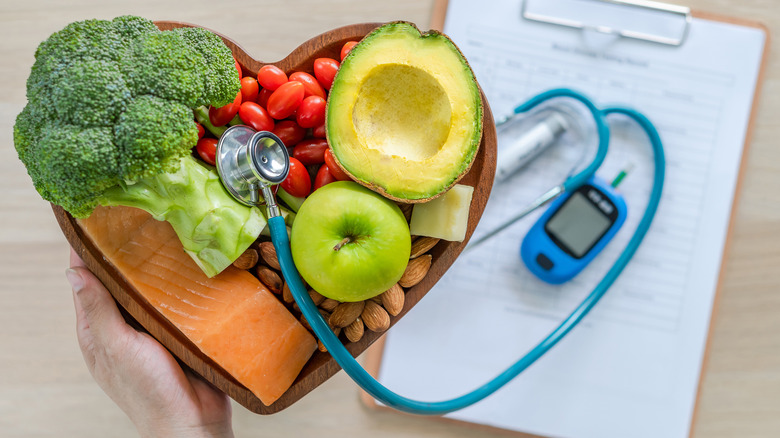 Fruits, veggies, nuts in heart-shaped bowl with stethoscope on top