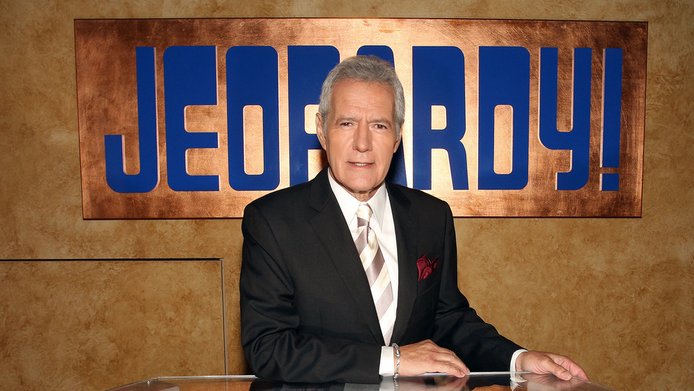 Alex Trebek posed in front of Jeopardy logo