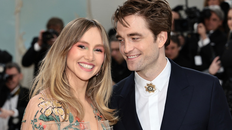 Robert Pattinson smiles and looks at smiling Suki Waterhouse