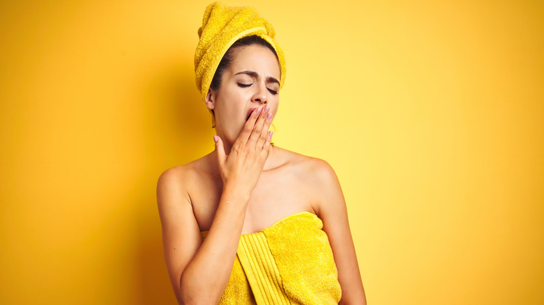 Woman wearing towel and yawning after cold shower