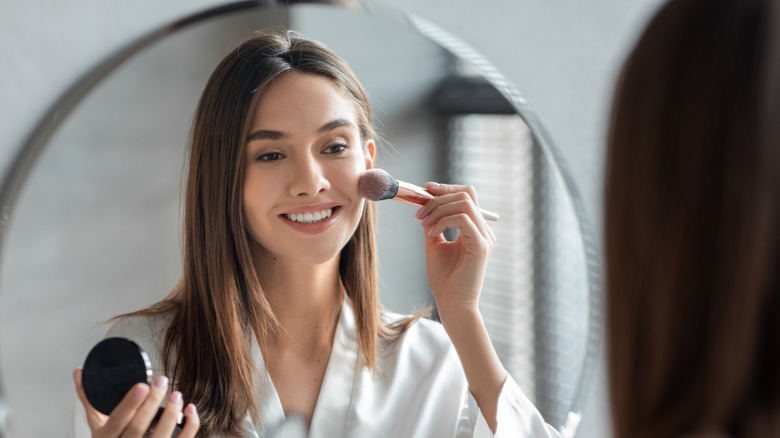 A woman applying blush to her face in the mirror