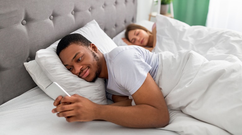 Man in bed with woman and texting someone else