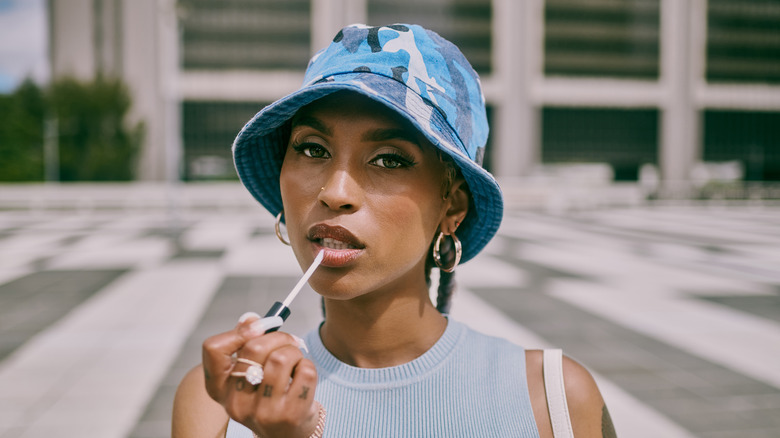 Woman in hat applying lipgloss