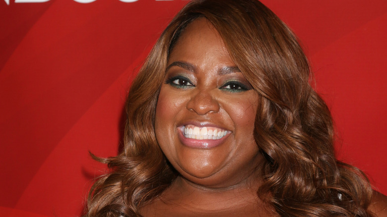 Sherri Shepherd poses with a smile against a red background.