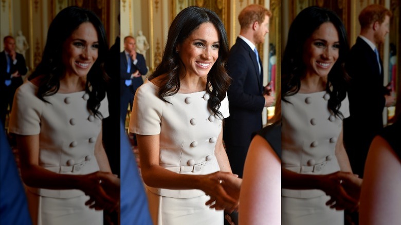 Meghan Markle smiling and shaking hands with woman