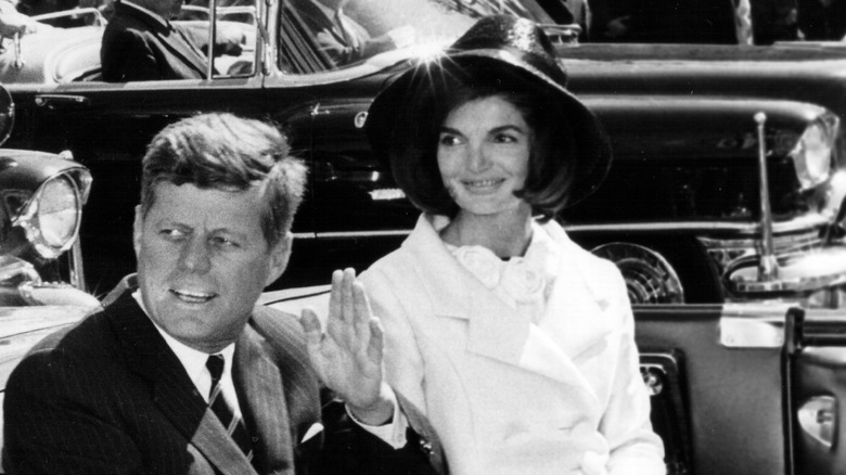 John F. Kennedy waving and Jackie Kennedy smiling in a parade 