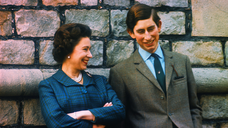 Charles and Queen Elizabeth posing against a wall 