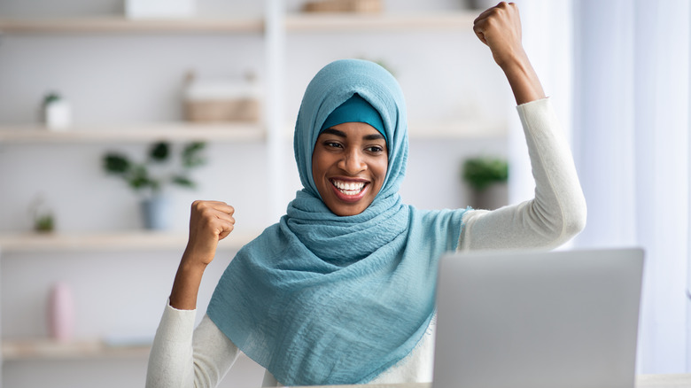 woman smiling wearing hijab with fists in the air celebrating