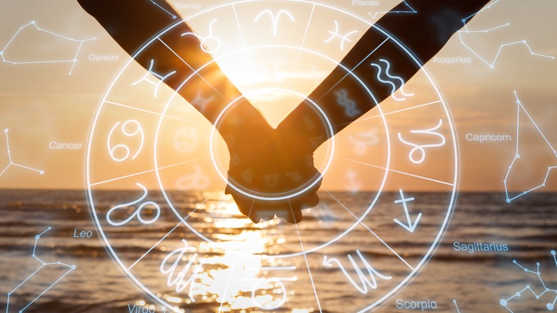 Two people holding hands behind the zodiac wheel 