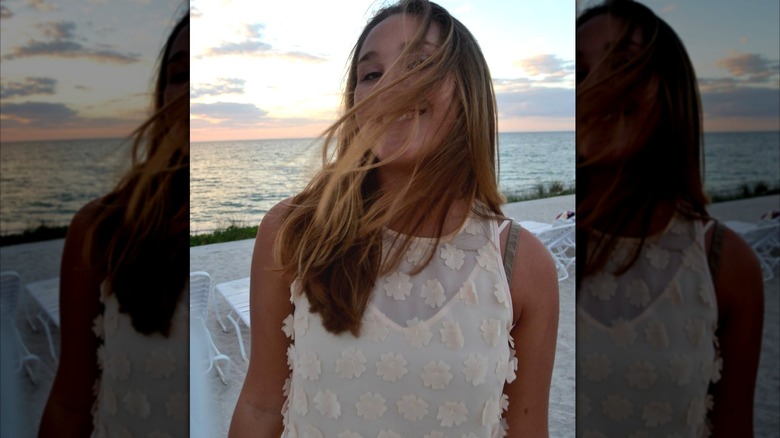 Lillie Carlson on a beach, hair blowing in smiling face, wearing a white top.