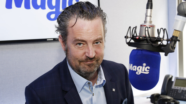 Matthew Perry looking serious in front of a microphone