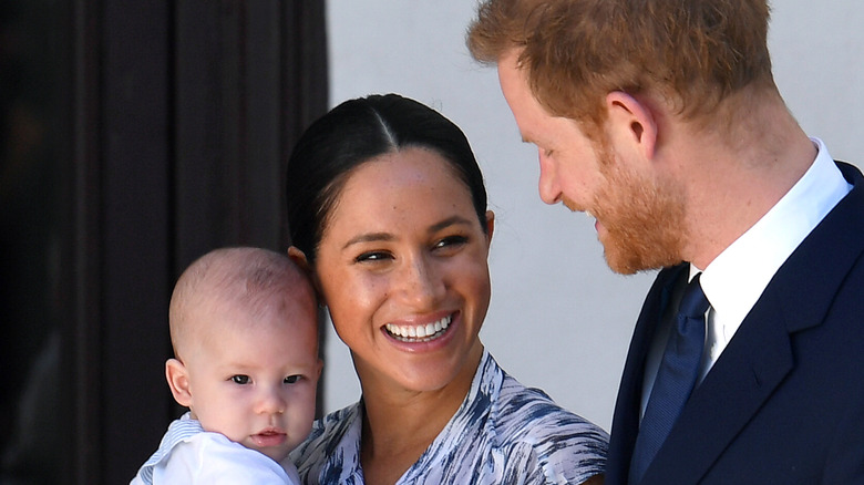 Meghan Markle holding Prince Archie and Prince Harry smiling at him