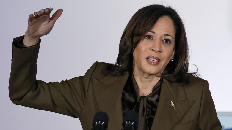 Kamala Harris, hand raised, speaks at a podium 