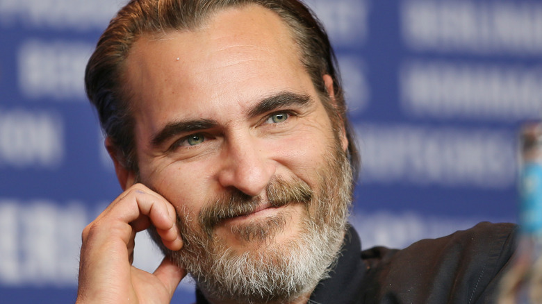 Joaquin Phoenix grinning with hand on face