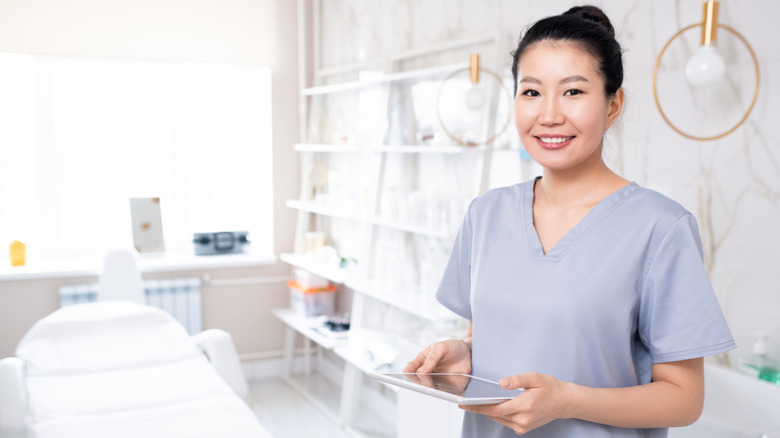 Smiling Asian healthcare professional in exam room holding tablet