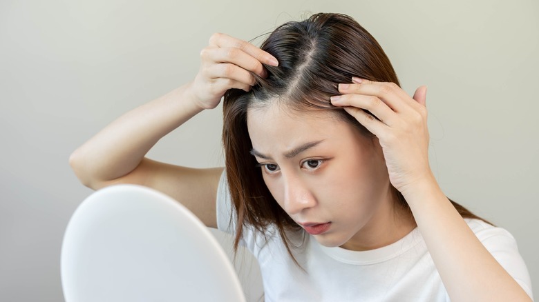 Concerned woman looking at her scalp in front of mirror