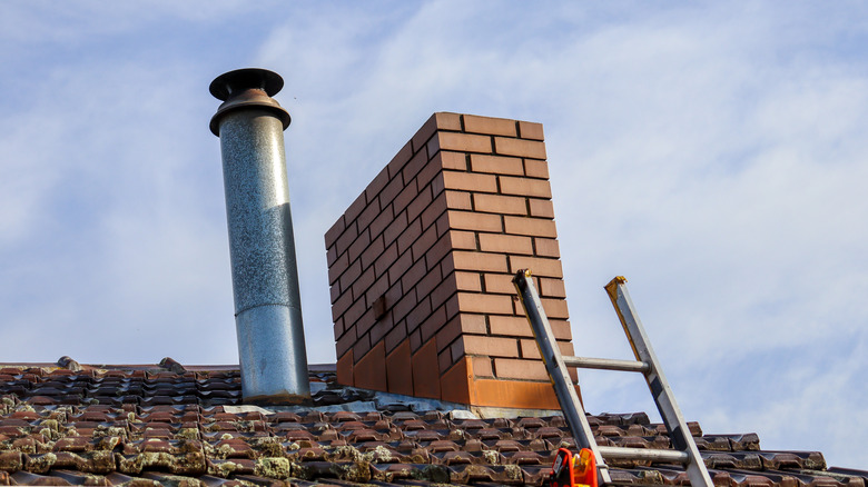 Metal and brick chimney with ladder leaning against roof 