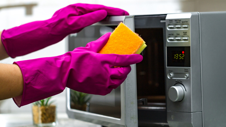 Person cleans microwave with sponge and pink rubber gloves