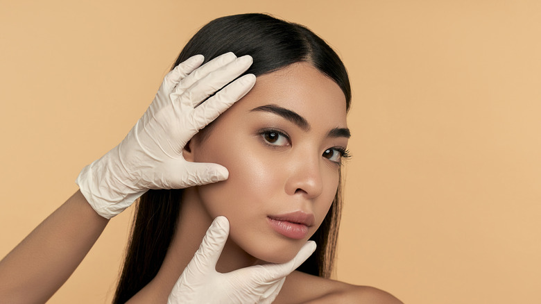 Gloved hands examining woman's face