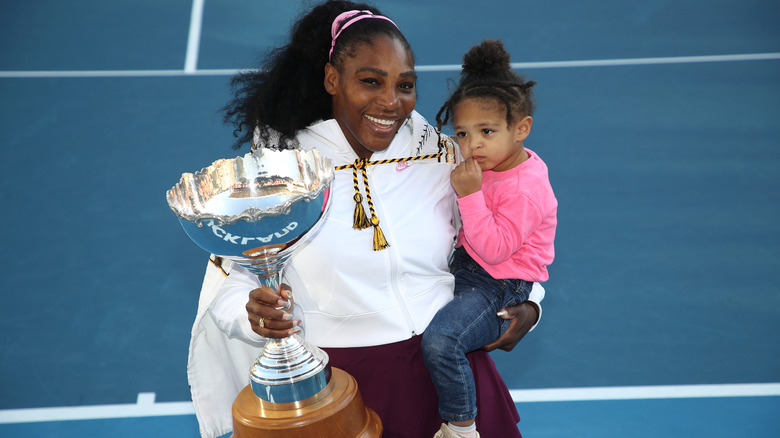 Serena Williams holding Olympia in one hand and a trophy in the other