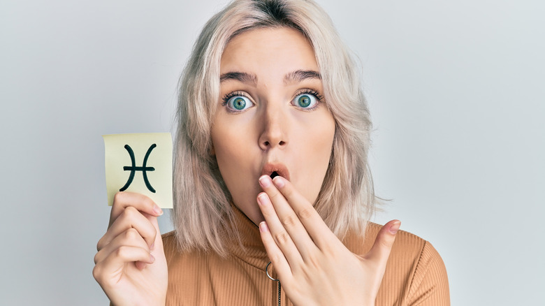 A woman holding a card with the Pisces zodiac sign on it. 