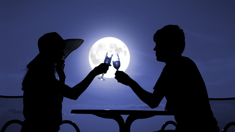 Two people clinking glasses in front of moon 