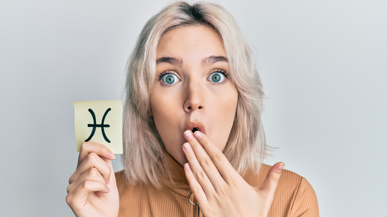 A woman holding a card with a Pisces sign on it 