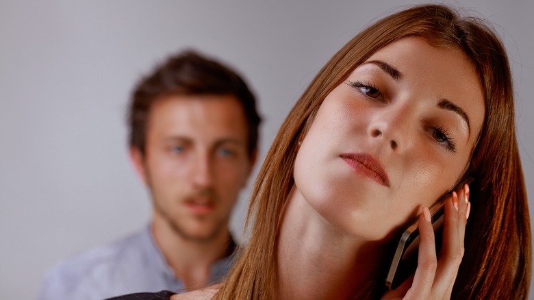 A woman talking on the phone while a man stands behind her