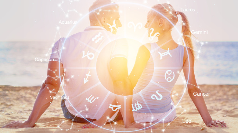 Couple holding hands on beach behind zodiac wheel