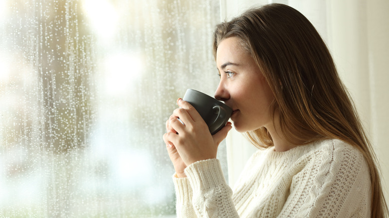 A woman drinking coffee and looking out the window. 