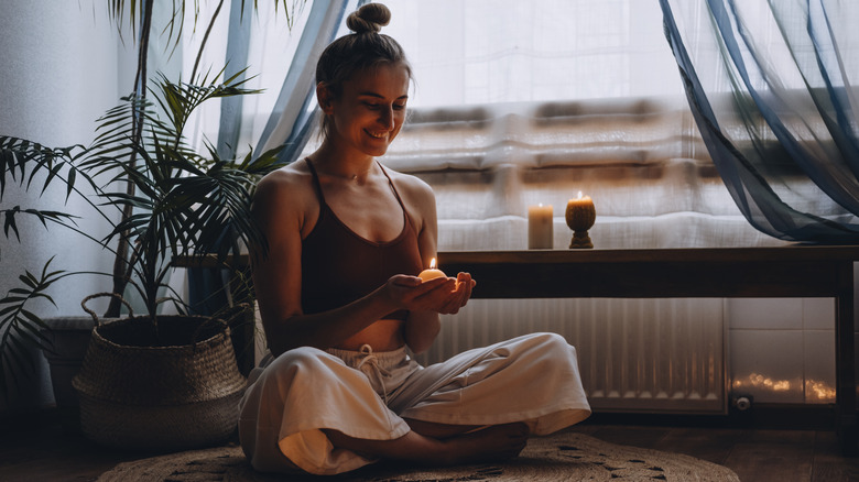 Woman smiling at hands holding candle, meditating