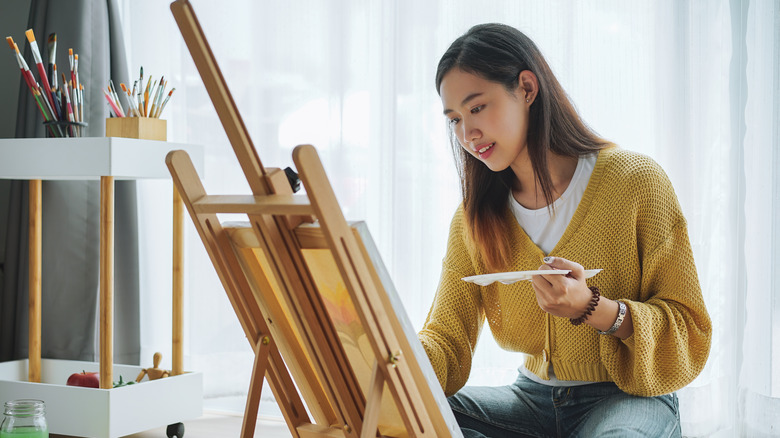 A woman painting near a window.