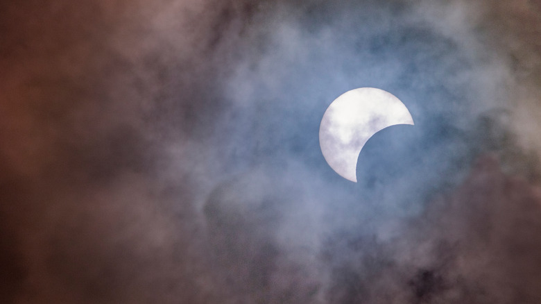 A partial solar eclipse surrounded by clouds