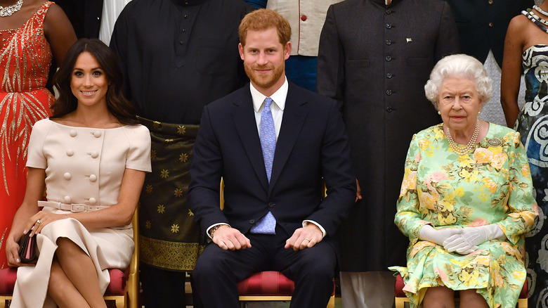 Meghan Markle, Prince Harry, and the queen sit together at an event