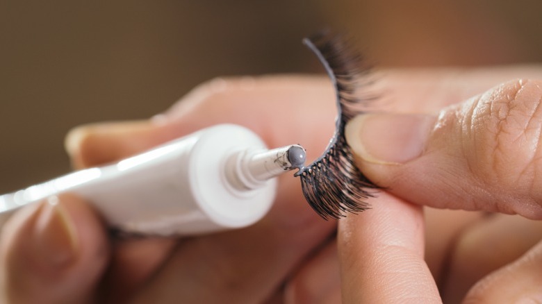 Person applying glue to false eyelash