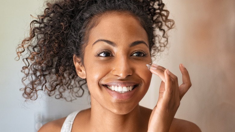 Smiling woman putting cream on her cheek