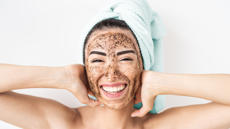 Woman with an exfoliator on her face and her hair in a towel