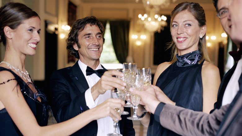 Men and women in formal outfits raising glasses